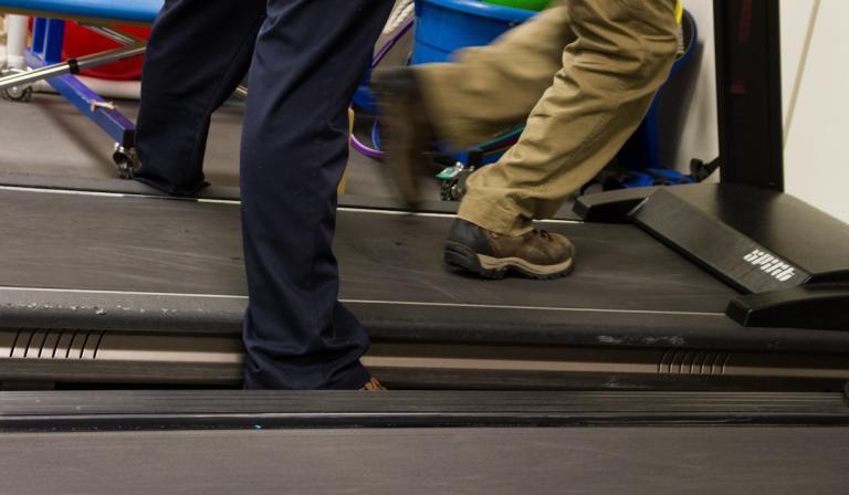 A physical therapist helping a child run on a treadmill.